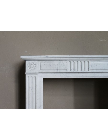 Grazioso camino antico neoclassico di piccola taglia in marmo bianco con dettagli scultorei floreali molto eleganti.
