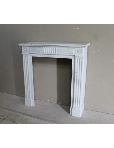 Grazioso camino antico neoclassico di piccola taglia in marmo bianco con dettagli scultorei floreali molto eleganti.