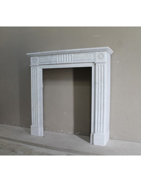 Grazioso camino antico neoclassico di piccola taglia in marmo bianco con dettagli scultorei floreali molto eleganti.