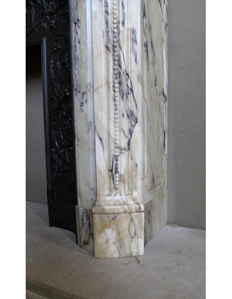 Camino neoclassico in marmo Statuario venato con toni dal bianco al beige al viola, provvisto di controcuore in ghisa d'origine.