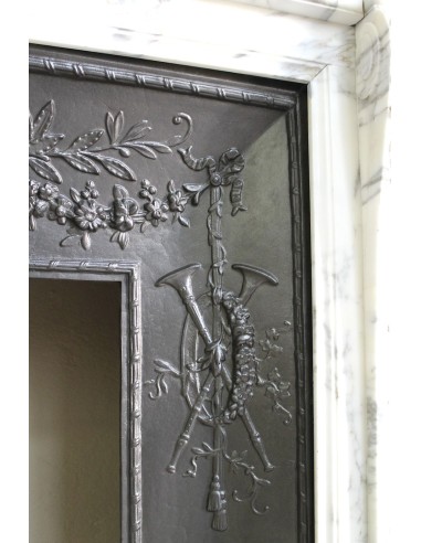 Camino neoclassico "Trois Fleurs" in marmo bianco venato Arabescato, provvisto di controcuore in ghisa artistica.