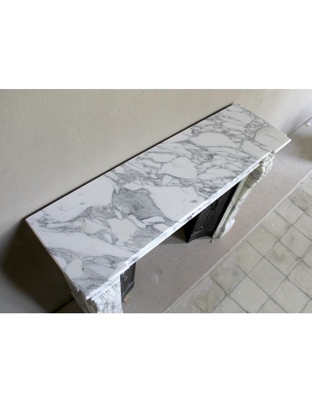 Camino neoclassico "Trois Fleurs" in marmo bianco venato Arabescato, provvisto di controcuore in ghisa artistica.