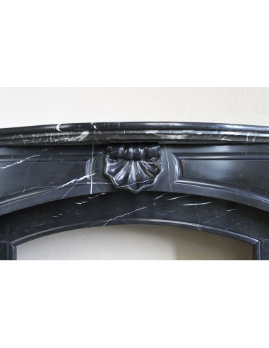 Camino antico di grandi dimensioni scolpito in nero marquinia, con venature bianche a contrasto, a decoro barocco di conchiglia.