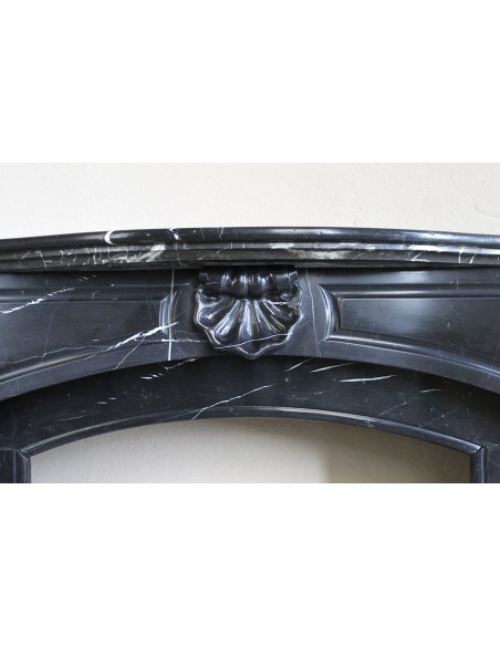 Camino antico di grandi dimensioni scolpito in nero marquinia, con venature bianche a contrasto, a decoro barocco di conchiglia.