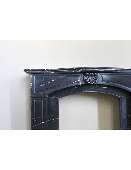 Camino antico di grandi dimensioni scolpito in nero marquinia, con venature bianche a contrasto, a decoro barocco di conchiglia.