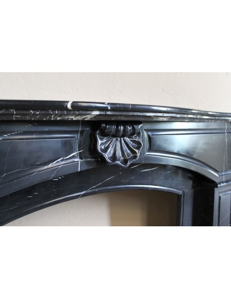 Camino antico di grandi dimensioni scolpito in nero marquinia, con venature bianche a contrasto, a decoro barocco di conchiglia.