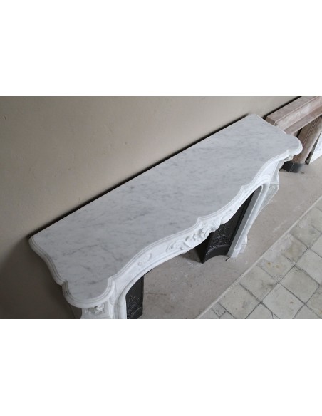 Camino barocco in marmo bianco Carrara con eleganti decori floreali provvisto di controcuore originale in ghisa artistica.