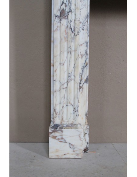 Camino neoclassico di piccola e graziosa taglia, scolpito in marmo Calacatta Oro Gold, con decori floreali.